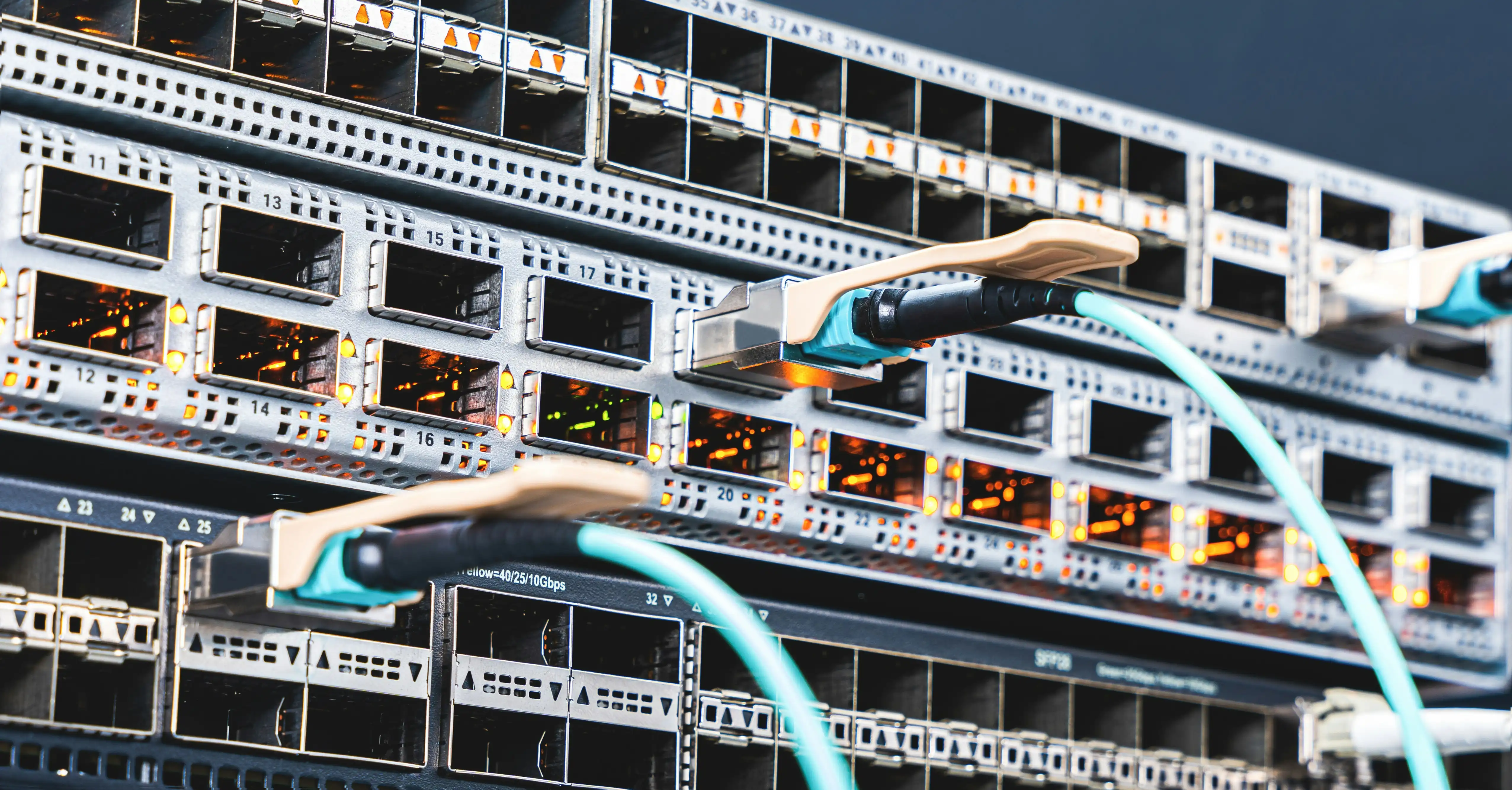 High-density network switch ports with teal fiber patch cables connected.