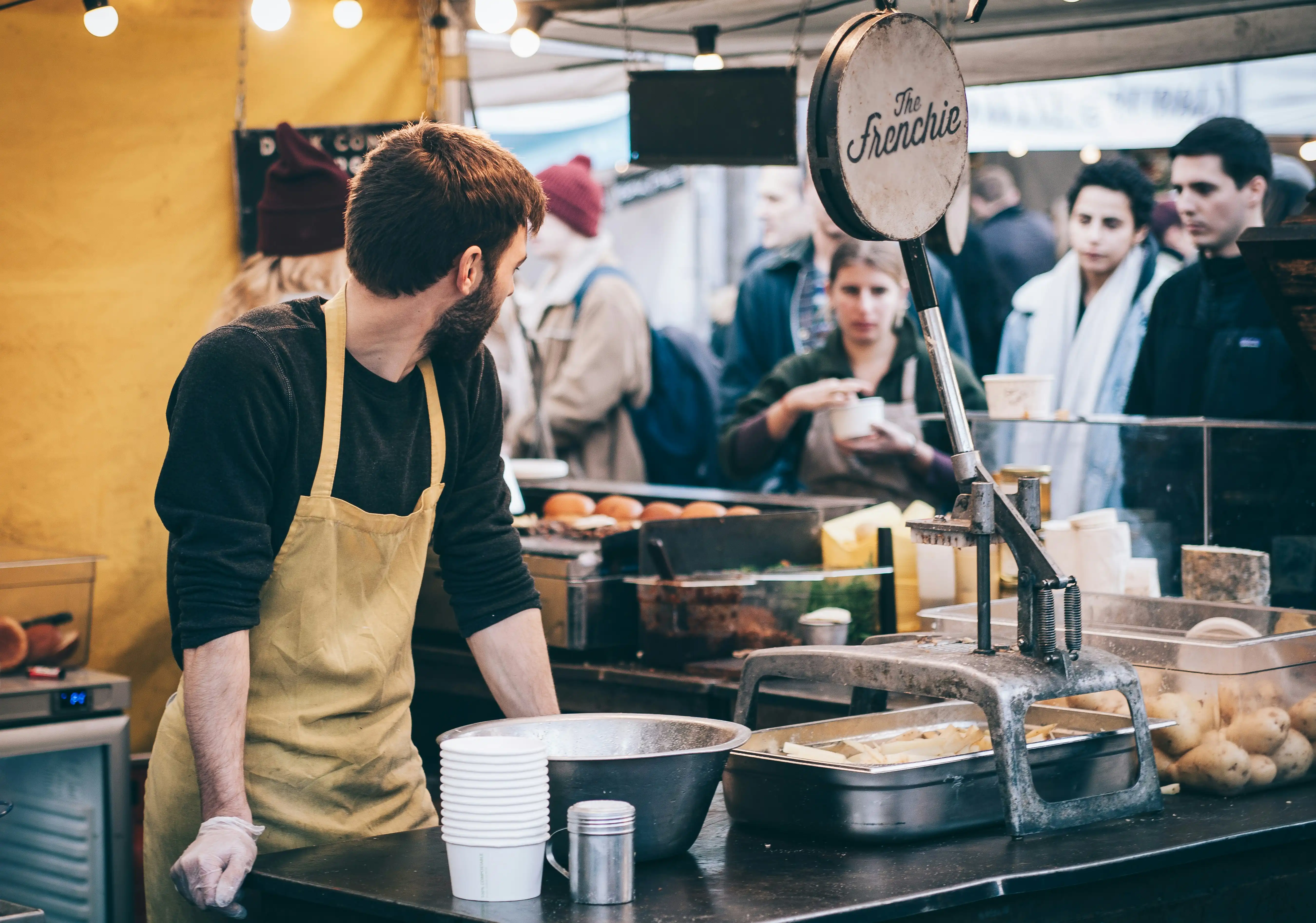 A vendor working a busy food-service counter at a market stall.