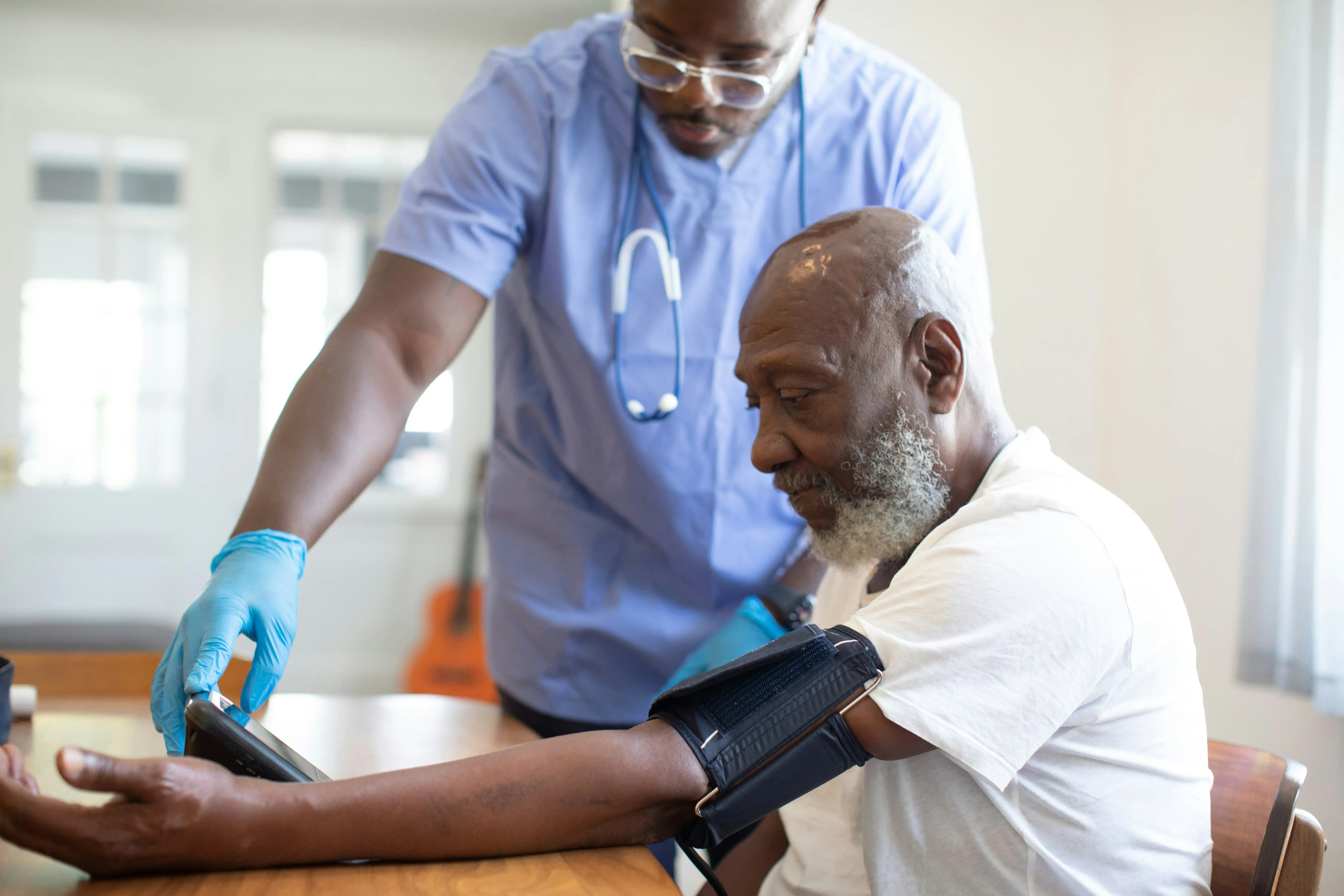 A nurse in scrubs taking an older patient’s blood pressure with a digital monitor.