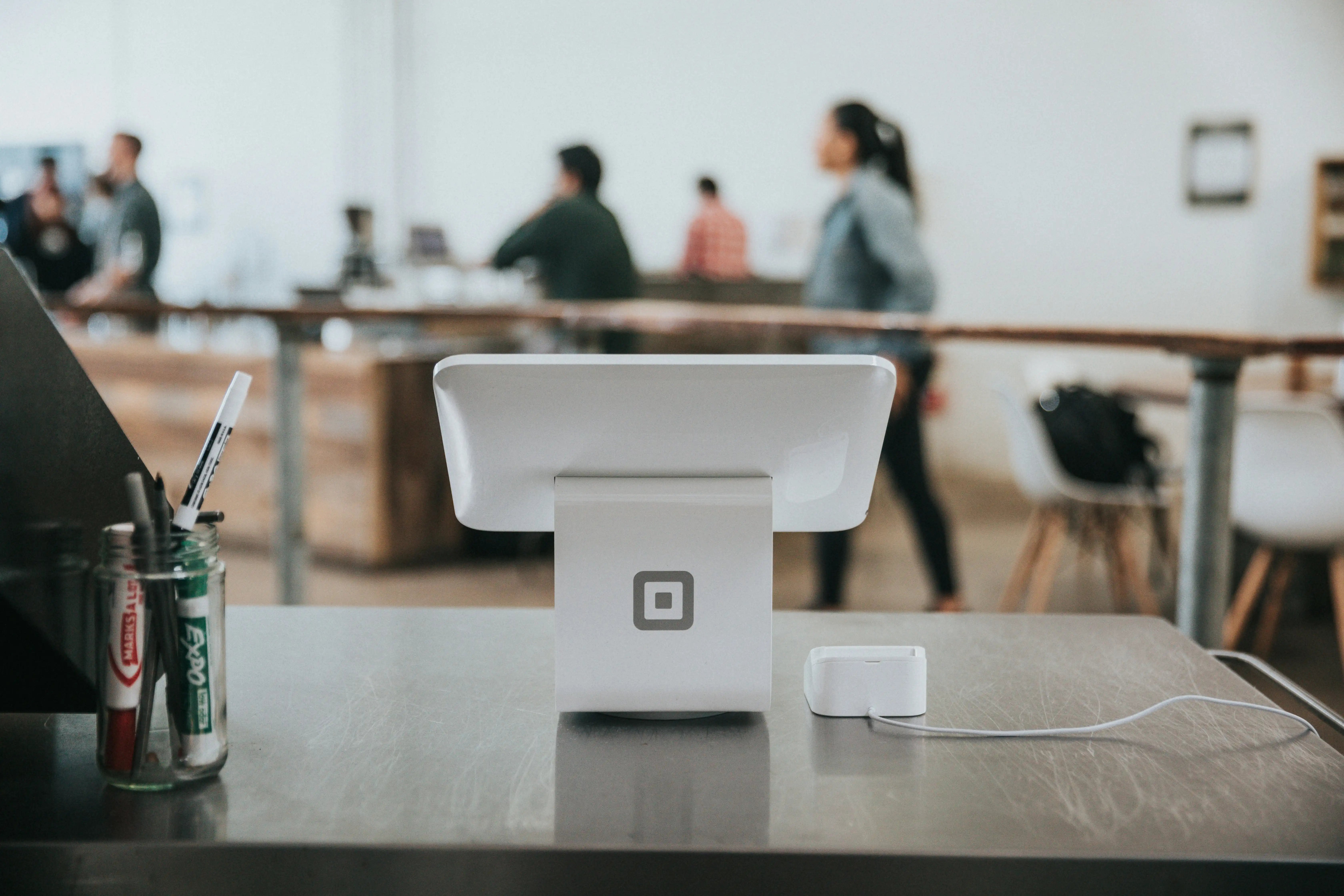 A countertop point-of-sale terminal in a retail store, staff and customers behind it.