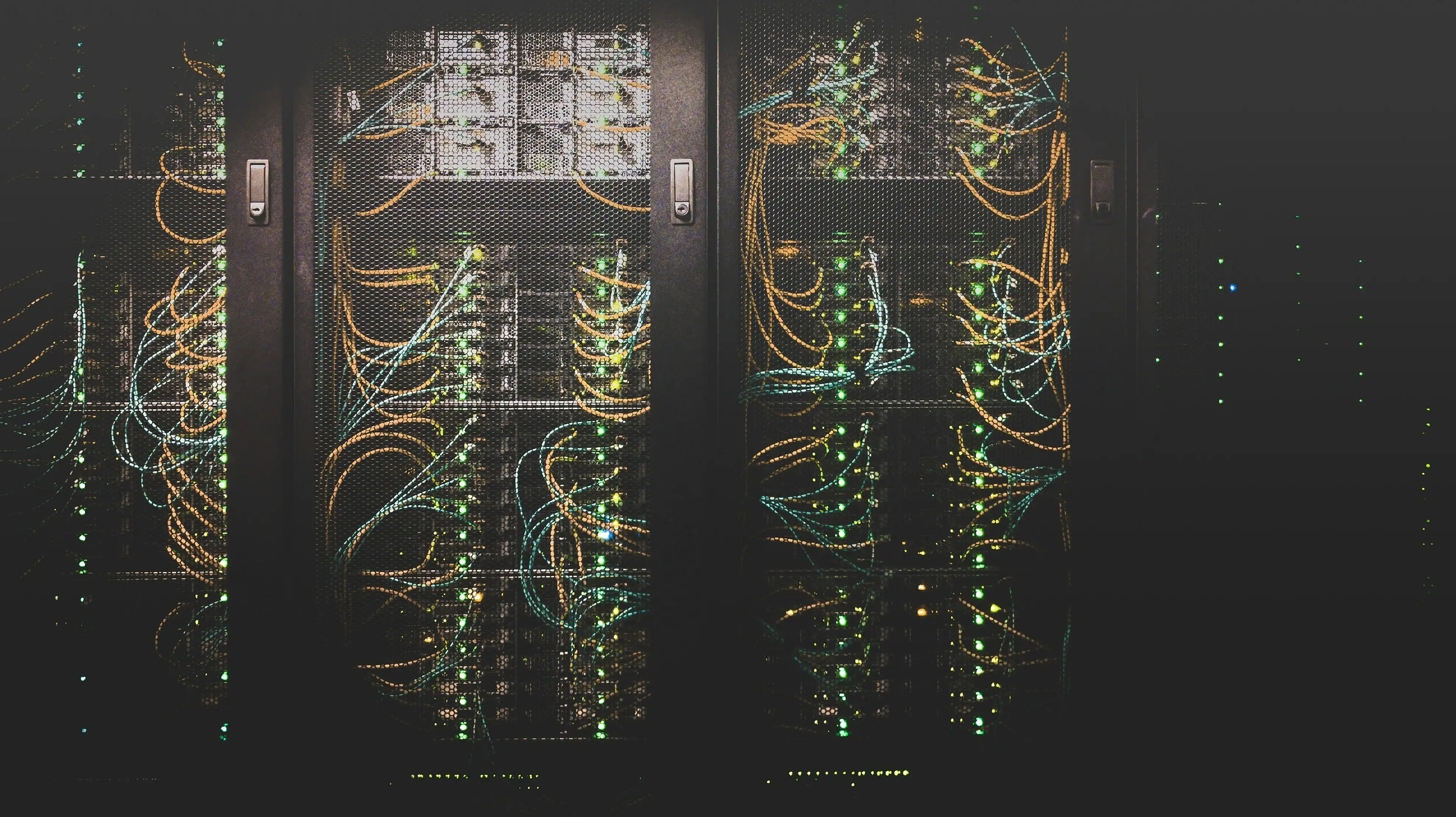 Rows of dark server racks threaded with orange and green network cabling in a data center.