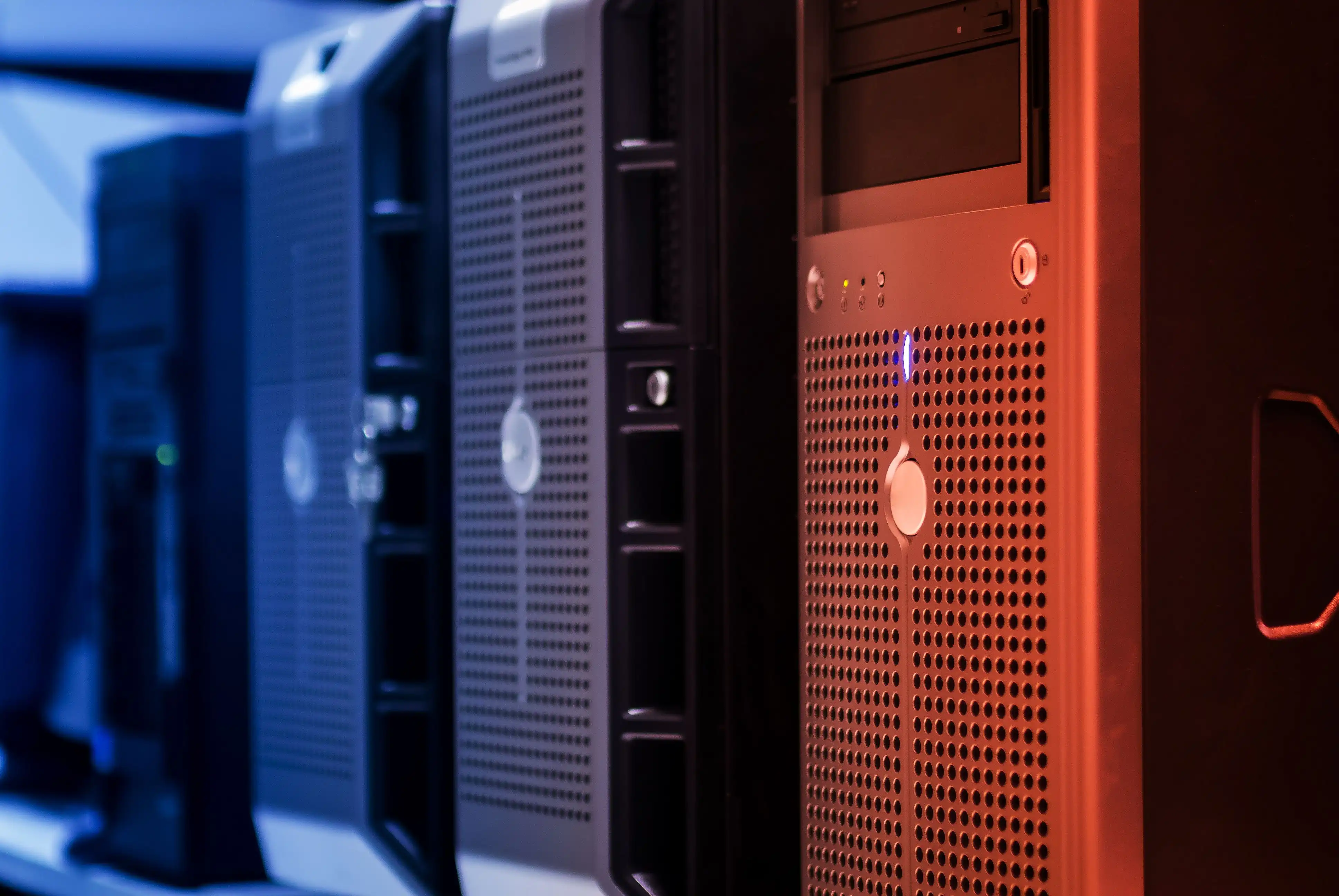 A row of tower servers lit in blue and red, shot at a shallow angle.